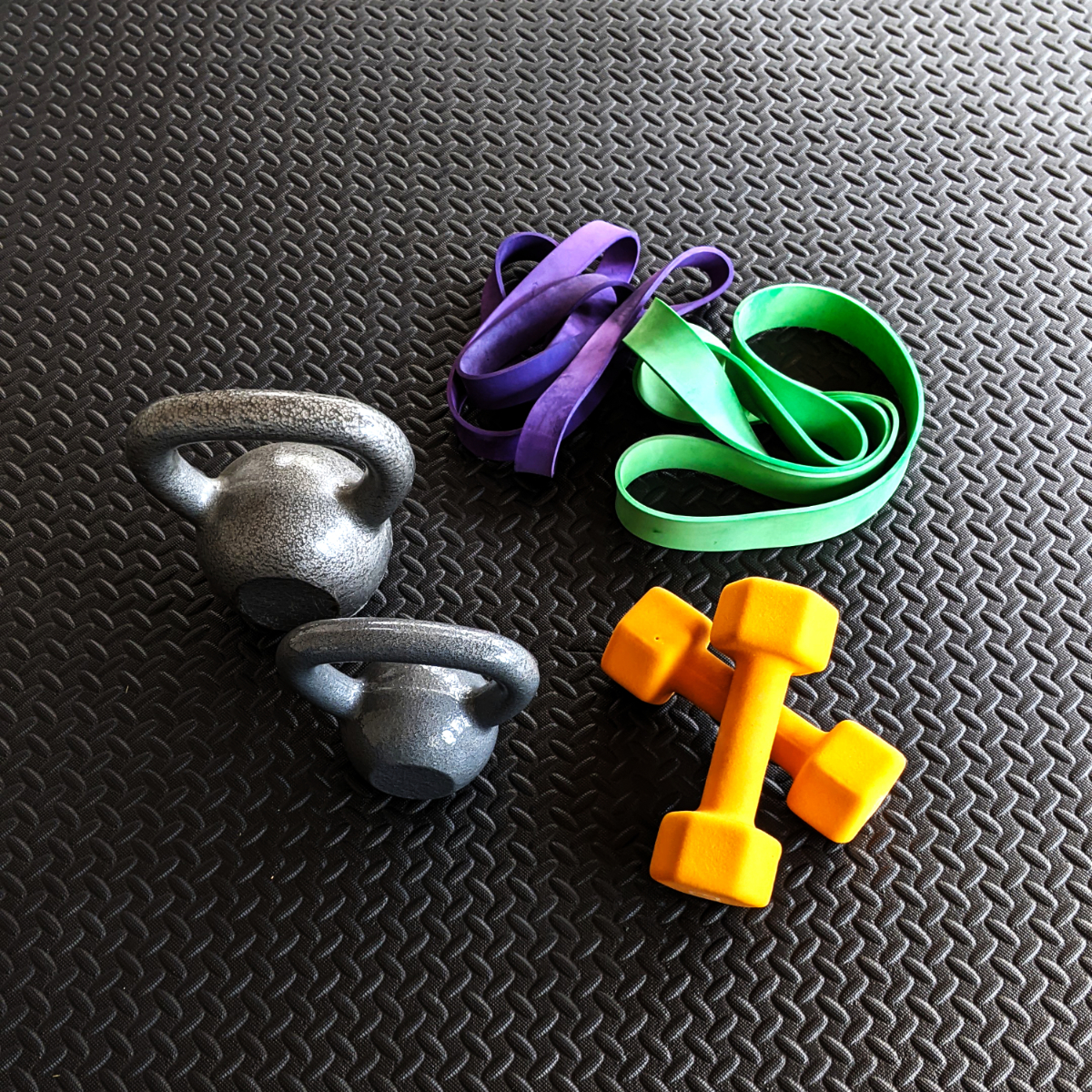 Strength training equipment, including orange dumbbells, kettlebells, and resistance bands, on a workout mat