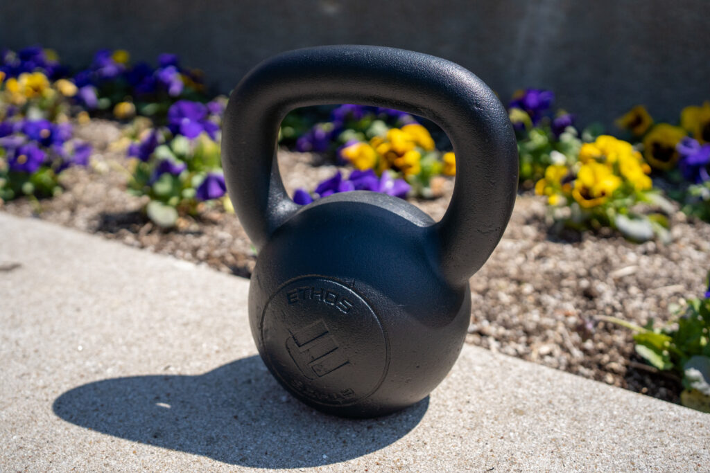 a kettebell sitting in front of a flower bed, ready for spring cleaning, fitness style