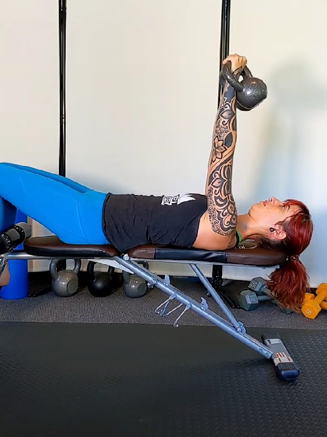 Woman demonstrating a kettlebell bench press, to help answer the question "Should I lift weights?"