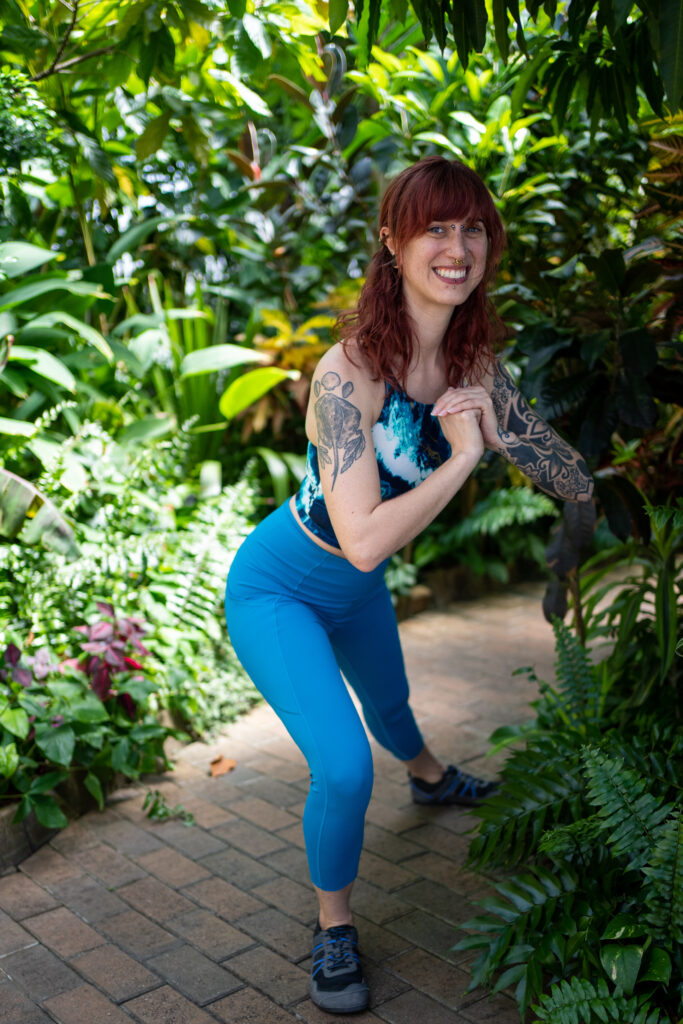Sarah, in blue workout gear, demonstrates an exercise modification for a squat.
